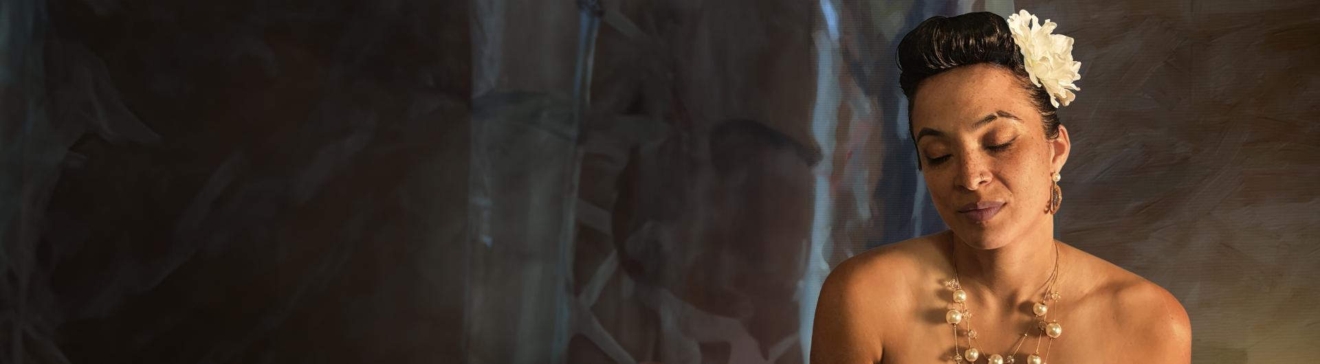 Kandace Springs wearing a necklace and a flower in her hair, eyes closed.