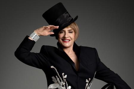 Patti LuPone wearing a top hat with one arm raised